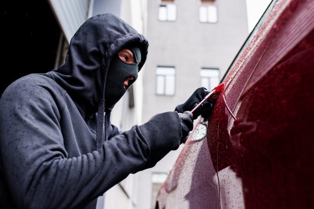 Selective focus of burglar using screwdriver while opening car door on urban street